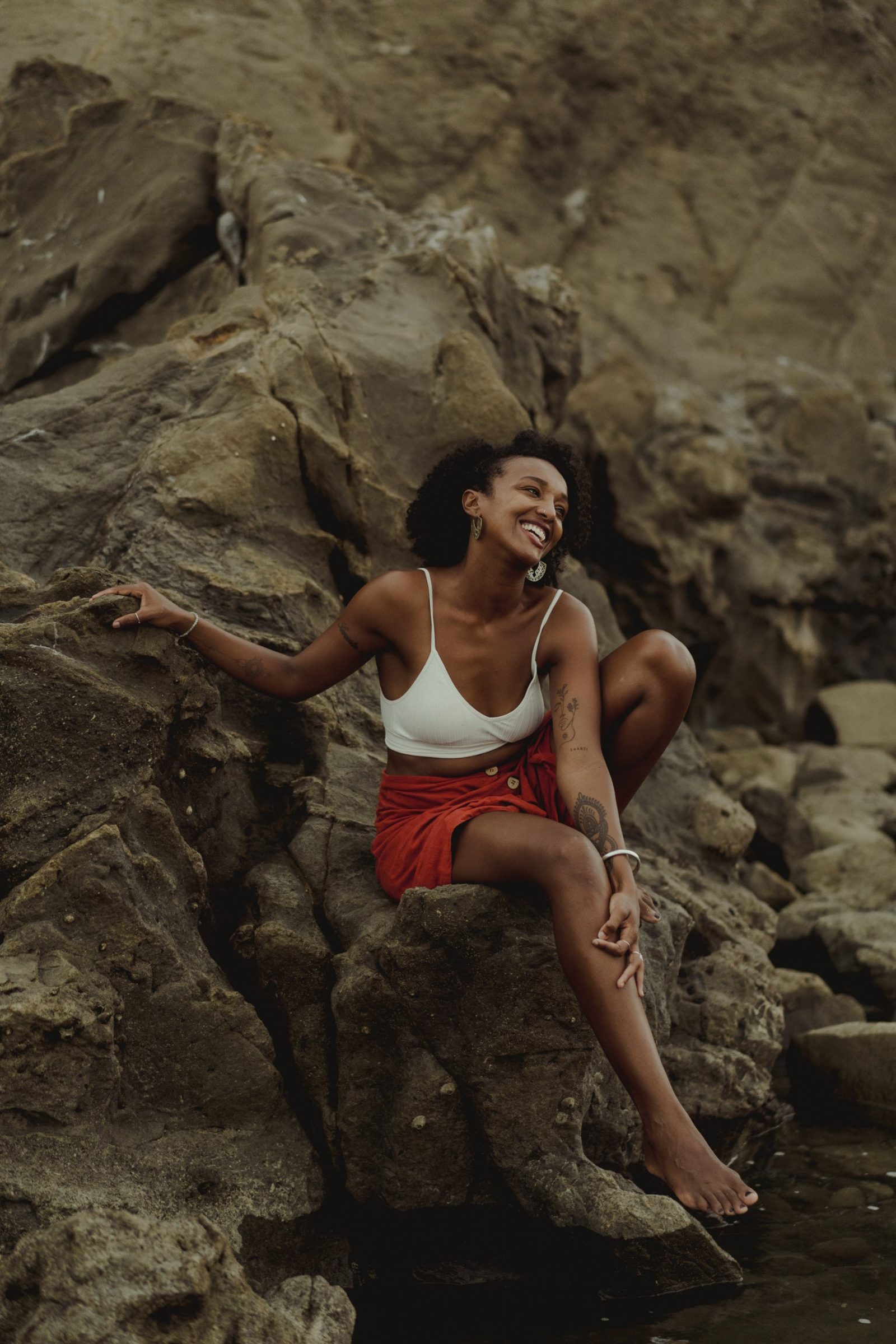 Badria laughing as she sits on the rocks by the sea