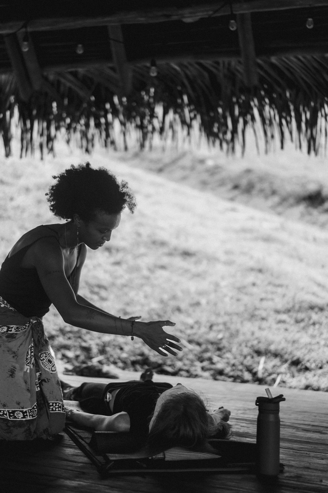 Black and white photo of Badria giving a bodywork session under a thatched roof