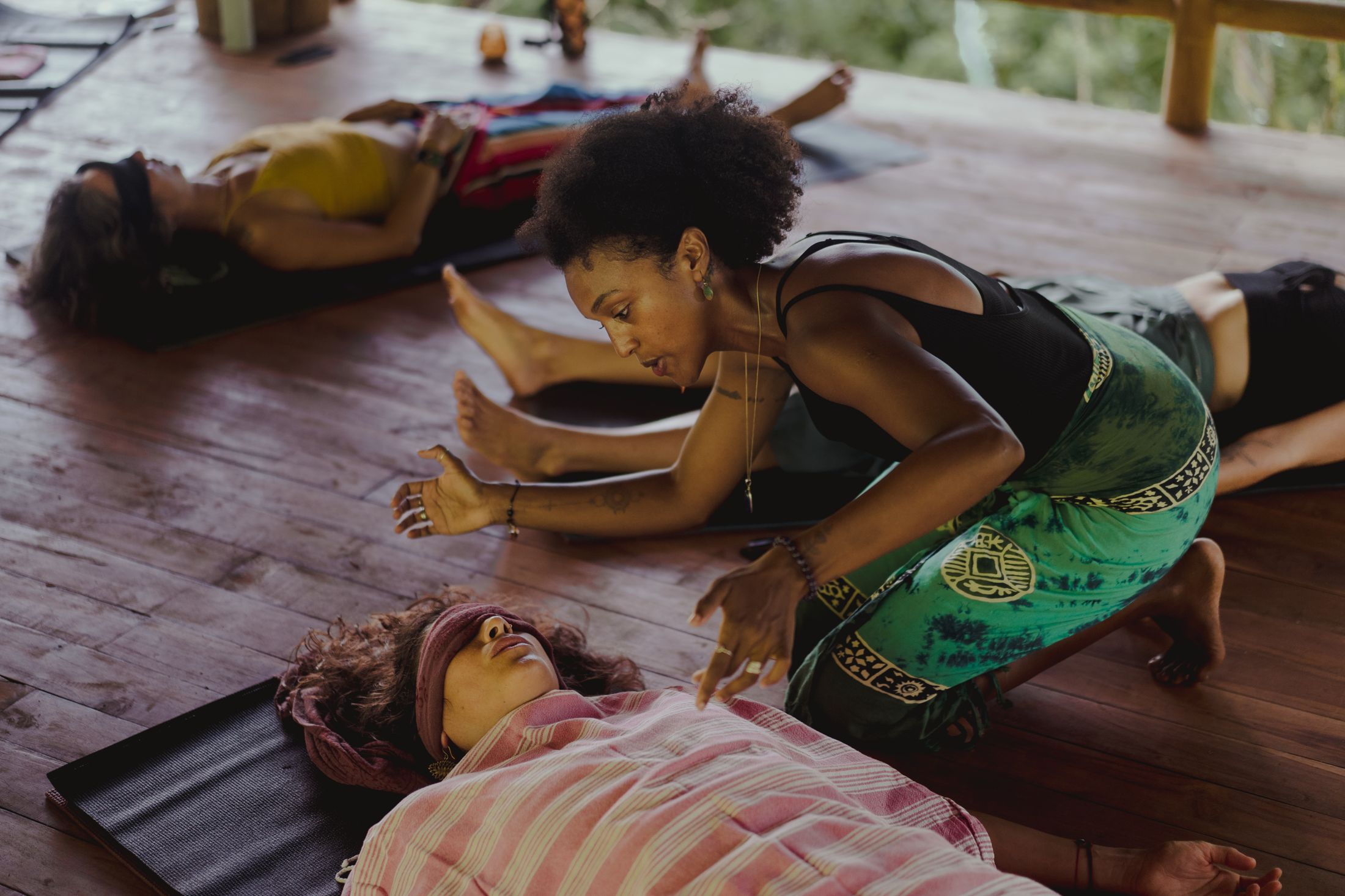 Badria guiding a somatic session on a wooden deck, clients lying on mats