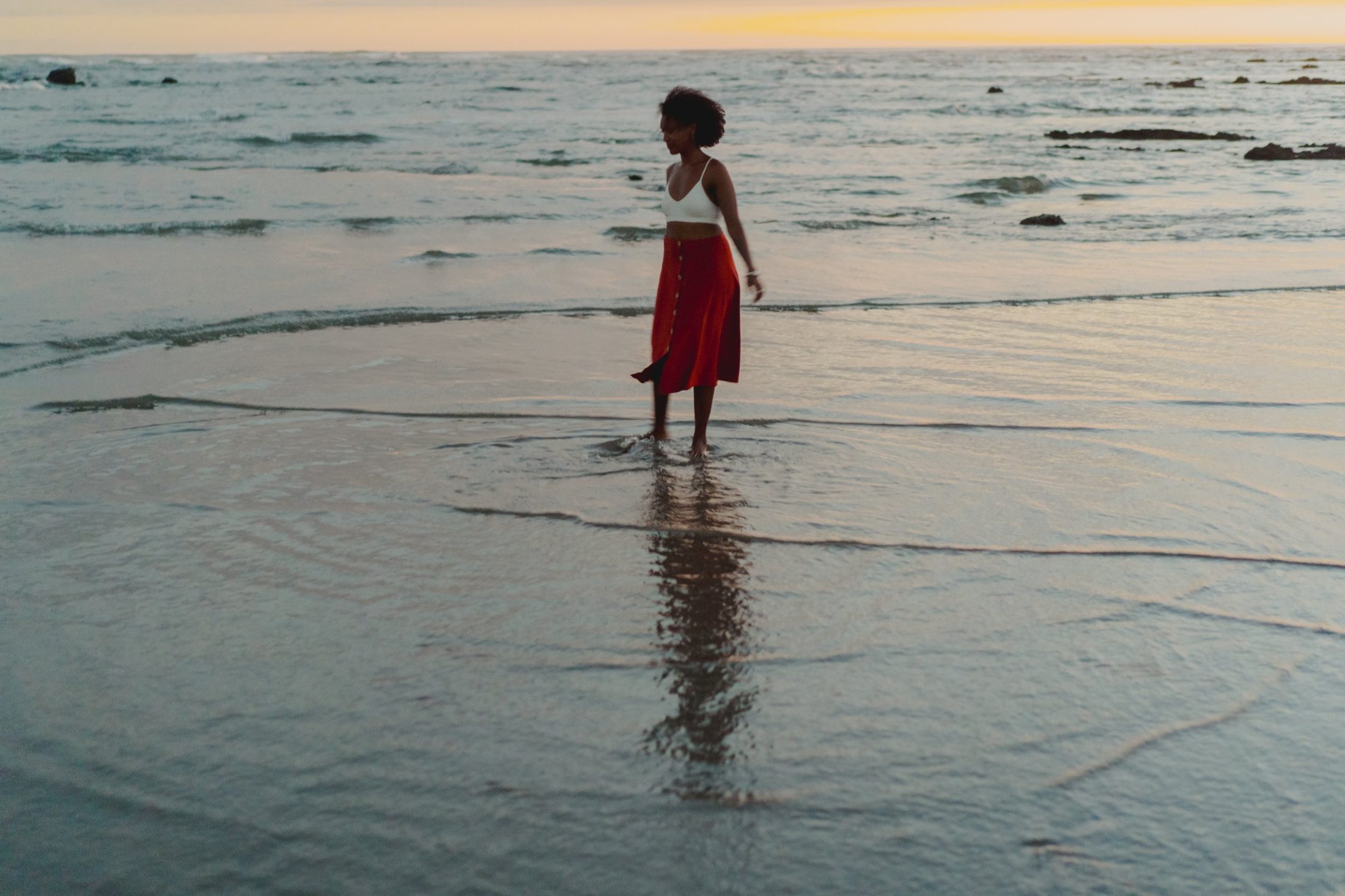 Badria walking barefoot at the edge of the sea at sunset