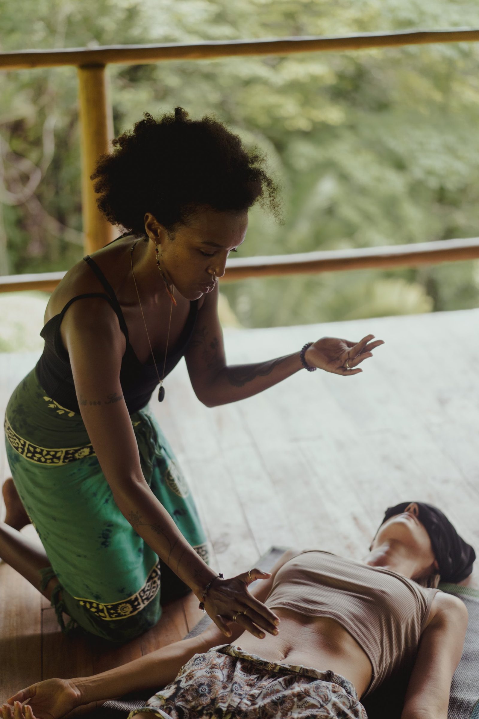 Badria kneeling beside a client, one hand resting on her belly and the other raised