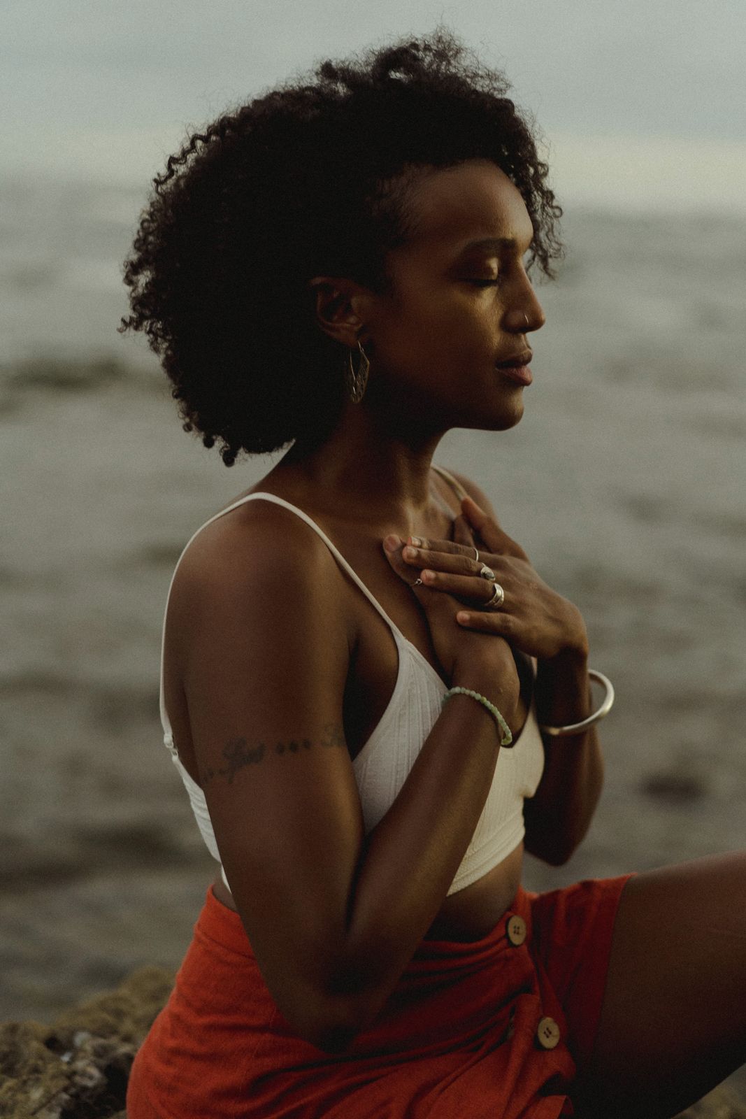 Badria sitting by the sea with her eyes closed and hands on her chest
