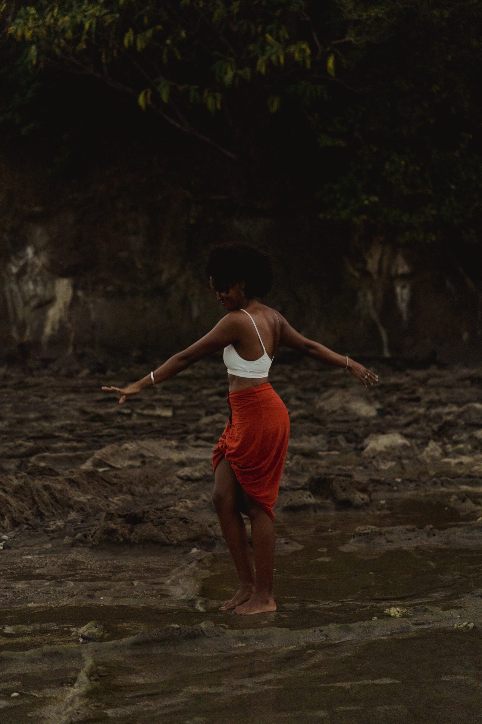 Badria dancing barefoot on the wet rocks by the sea, arms open